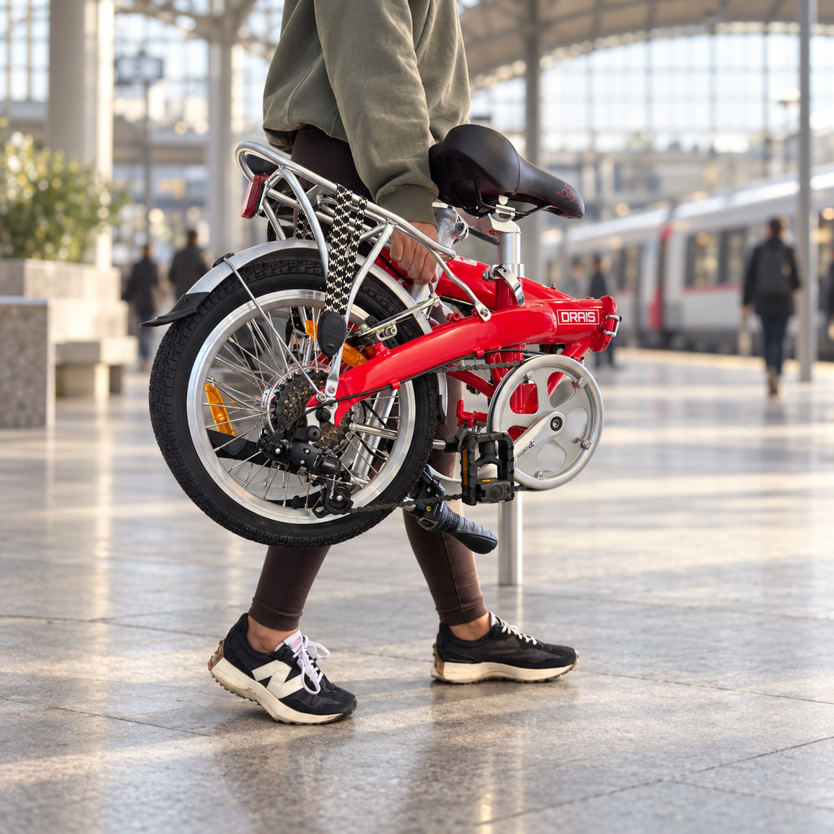 Commuter carrying a folded red Drais F16 bicycle through a railway station.